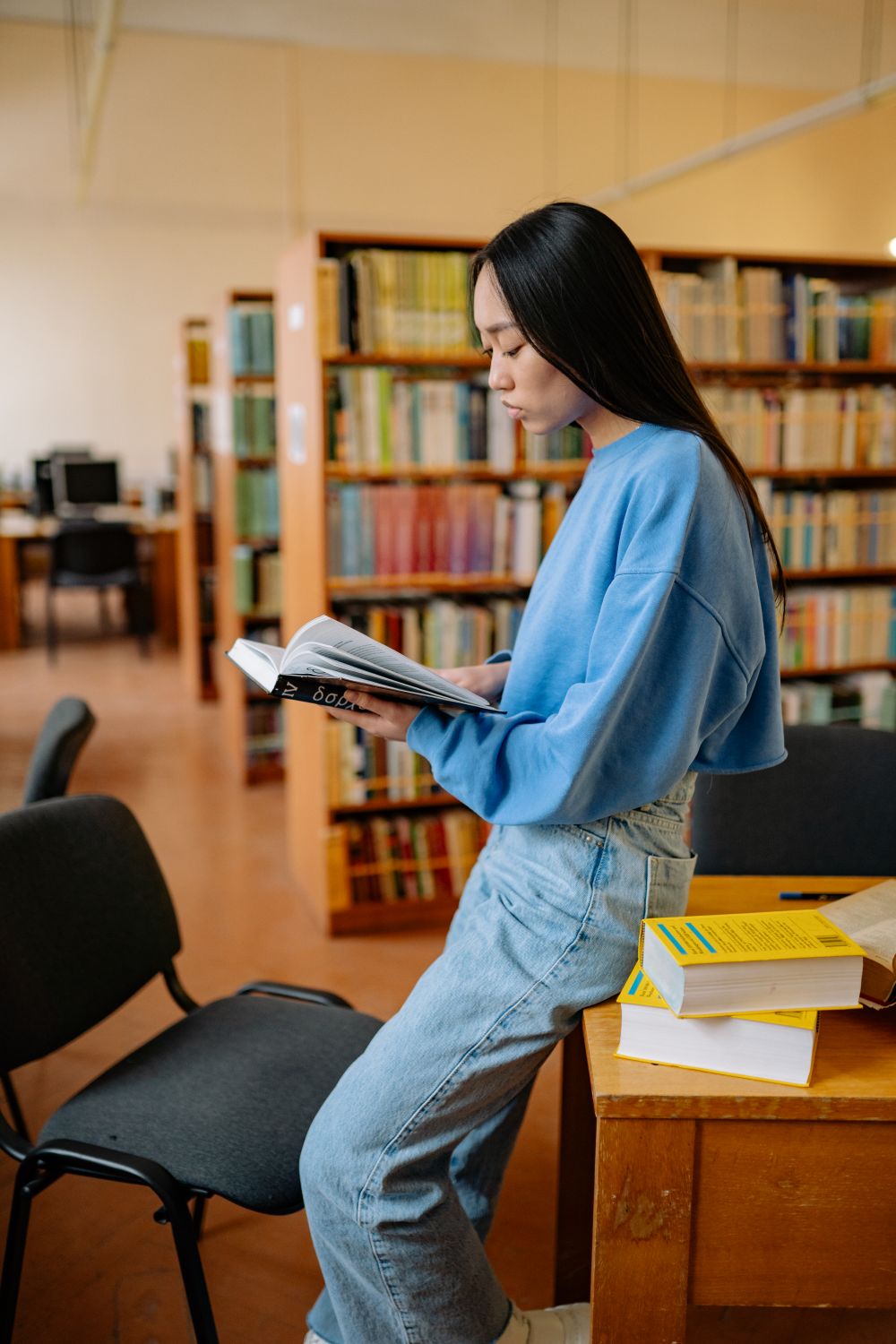 Student reading in a library surrounded by books